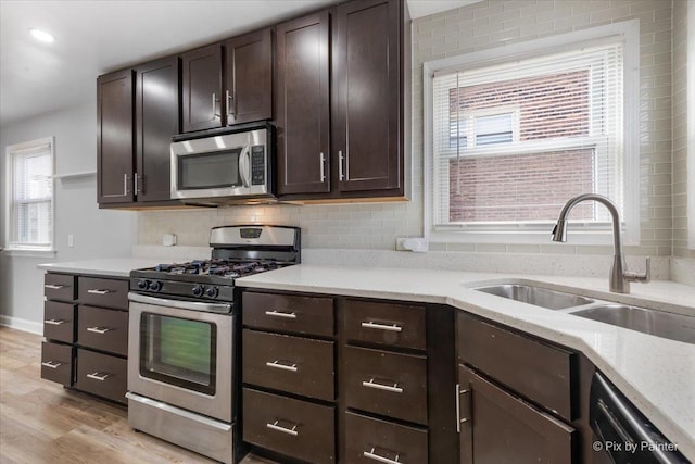 kitchen featuring dark brown cabinetry, stainless steel appliances, a sink, light wood-type flooring, and decorative backsplash