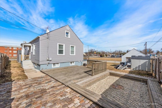 back of property with an outbuilding, a storage shed, a deck, and fence