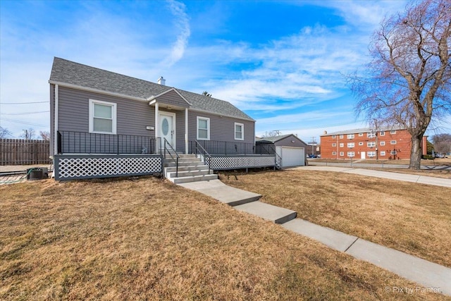 view of front of house featuring concrete driveway, a detached garage, an outbuilding, fence, and a front lawn