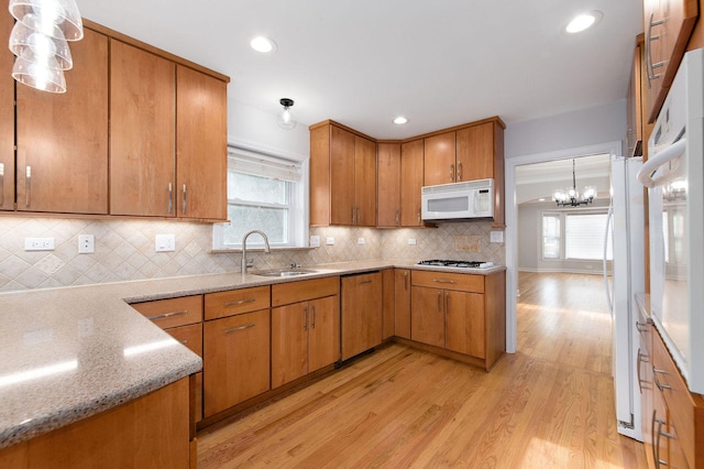 kitchen featuring pendant lighting, tasteful backsplash, sink, light hardwood / wood-style floors, and white appliances