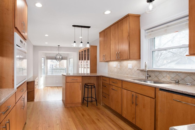 kitchen featuring pendant lighting, sink, white oven, tasteful backsplash, and light hardwood / wood-style floors