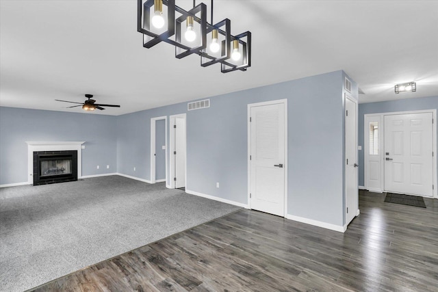 unfurnished living room with dark wood-style flooring, a fireplace with flush hearth, a ceiling fan, visible vents, and baseboards