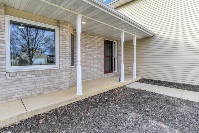 doorway to property featuring covered porch and brick siding