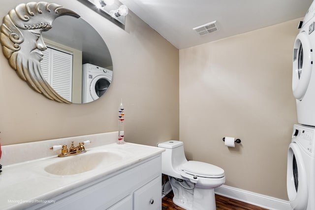 bathroom featuring vanity, wood finished floors, visible vents, baseboards, and stacked washer and clothes dryer