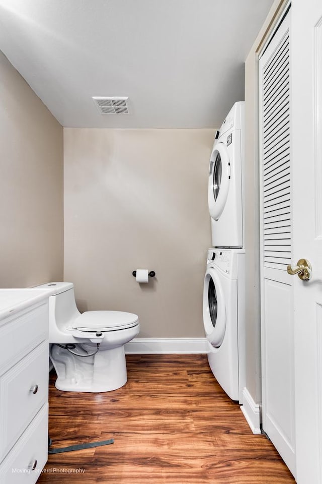 laundry area featuring visible vents, stacked washer and clothes dryer, light wood-style flooring, baseboards, and laundry area