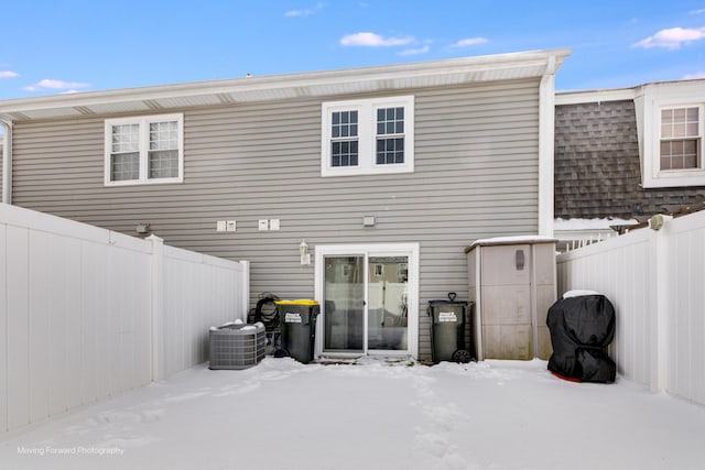 snow covered property featuring central air condition unit, fence, and a shingled roof