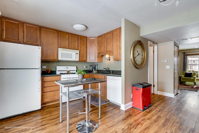 kitchen with white appliances, wood finished floors, baseboards, dark countertops, and brown cabinets