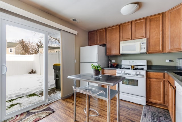 kitchen featuring visible vents, brown cabinets, dark countertops, wood finished floors, and white appliances