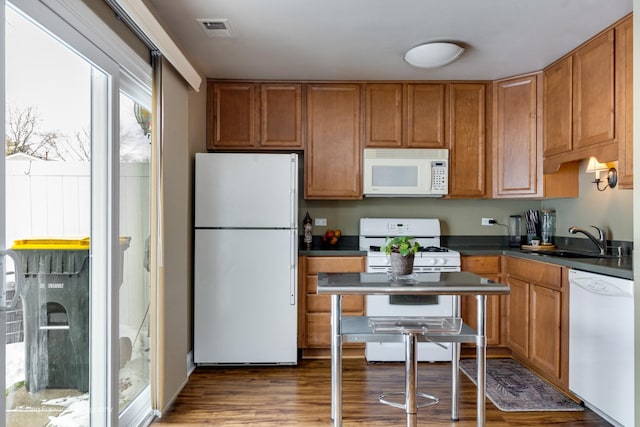 kitchen with visible vents, a sink, dark countertops, wood finished floors, and white appliances