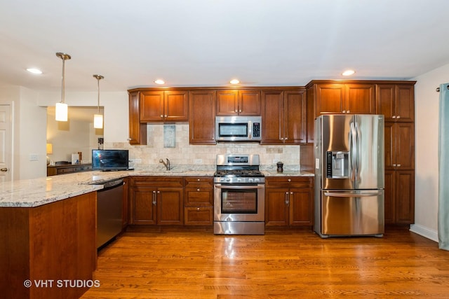 kitchen with dark wood-type flooring, hanging light fixtures, stainless steel appliances, light stone countertops, and kitchen peninsula