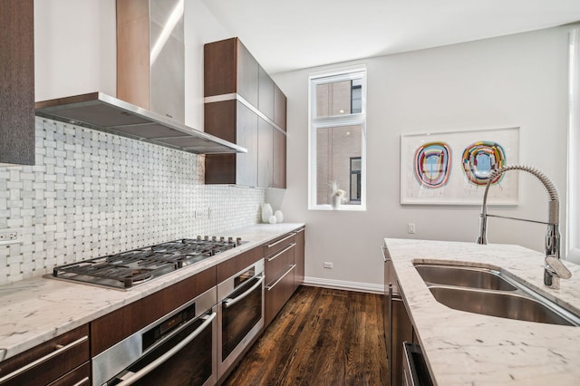 kitchen featuring sink, wall chimney range hood, stainless steel appliances, light stone countertops, and backsplash