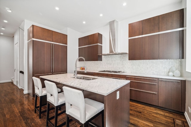 kitchen featuring sink, a breakfast bar area, dark hardwood / wood-style floors, an island with sink, and wall chimney range hood