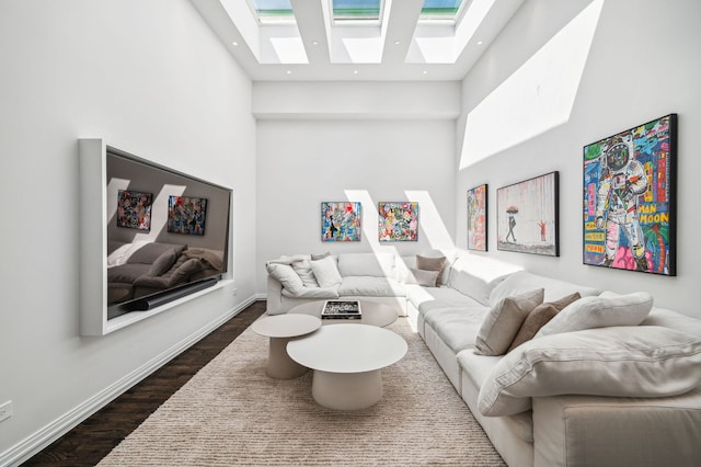 living room with a towering ceiling, a skylight, and dark hardwood / wood-style floors