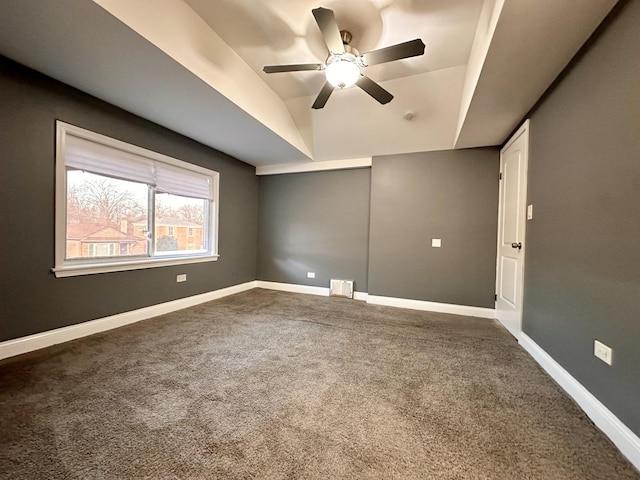 carpeted spare room featuring a tray ceiling, vaulted ceiling, and ceiling fan