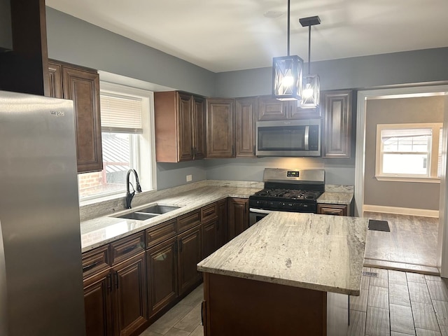 kitchen featuring sink, hanging light fixtures, a center island, stainless steel appliances, and light stone countertops