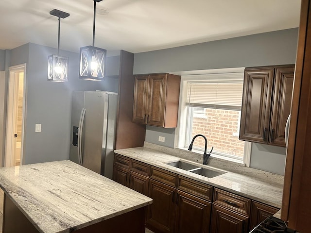 kitchen with sink, a center island, stainless steel refrigerator with ice dispenser, light stone countertops, and decorative light fixtures