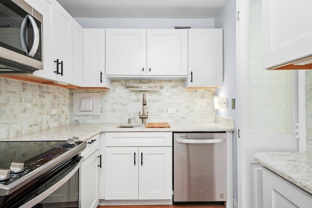 kitchen with tasteful backsplash, sink, white cabinets, stainless steel appliances, and light stone countertops