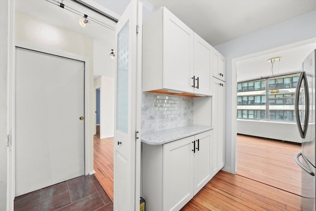 kitchen featuring white cabinetry, wood-type flooring, stainless steel fridge, and tasteful backsplash