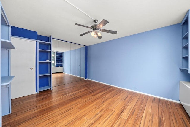 unfurnished living room featuring hardwood / wood-style flooring, built in shelves, and ceiling fan