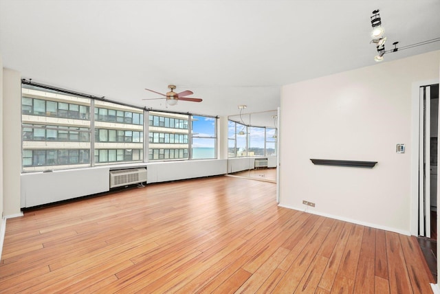 unfurnished living room with a wall mounted AC, ceiling fan, and light wood-type flooring