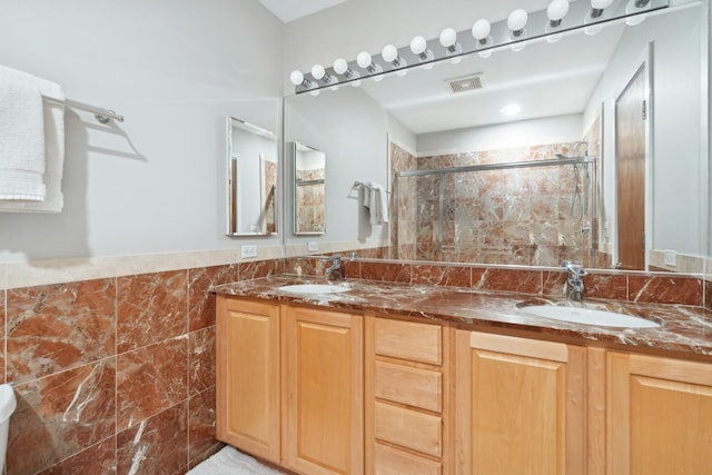 bathroom featuring tile walls, a shower stall, visible vents, and a sink