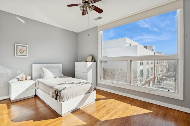 bedroom with a ceiling fan, wood finished floors, visible vents, and baseboards