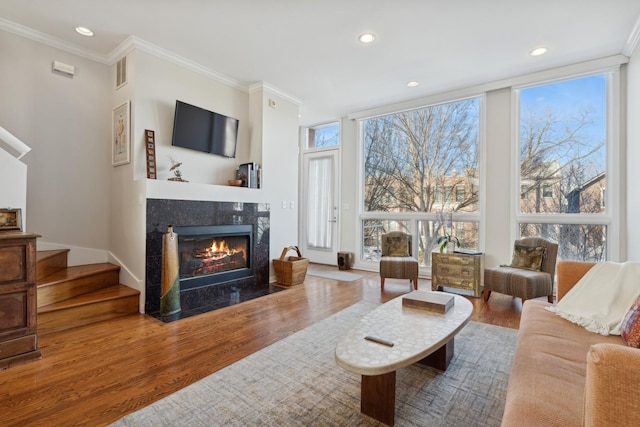 living area featuring floor to ceiling windows, a fireplace, ornamental molding, wood finished floors, and stairs