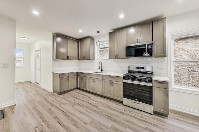 kitchen featuring appliances with stainless steel finishes, a wealth of natural light, sink, hanging light fixtures, and light hardwood / wood-style floors