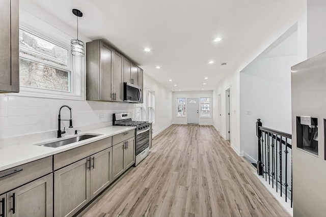 kitchen featuring sink, tasteful backsplash, pendant lighting, stainless steel appliances, and light hardwood / wood-style floors