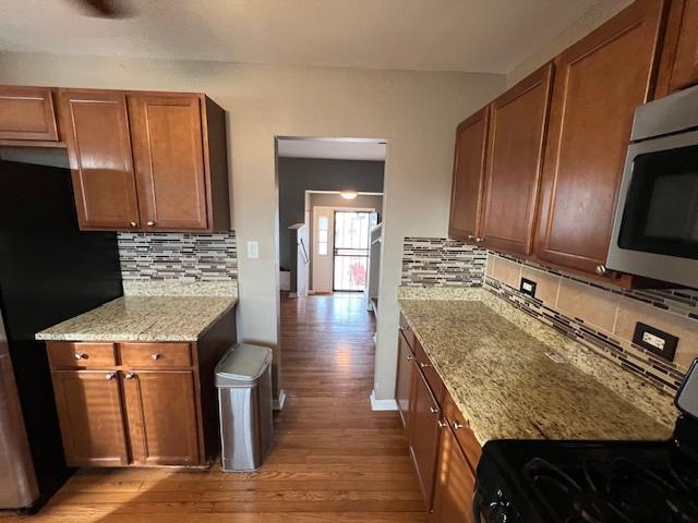 kitchen with stove, black refrigerator, light stone counters, and light hardwood / wood-style floors