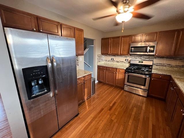 kitchen with appliances with stainless steel finishes, light stone counters, light hardwood / wood-style floors, and decorative backsplash