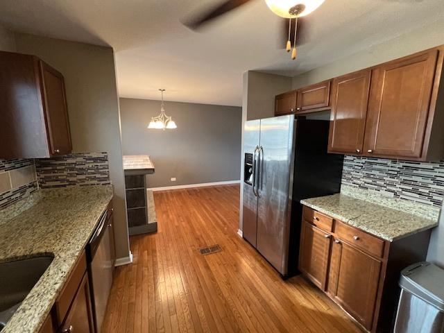 kitchen featuring hanging light fixtures, appliances with stainless steel finishes, light wood-type flooring, and light stone counters