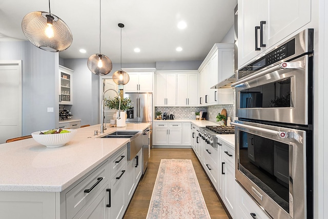 kitchen featuring stainless steel appliances, decorative light fixtures, a center island with sink, and white cabinets