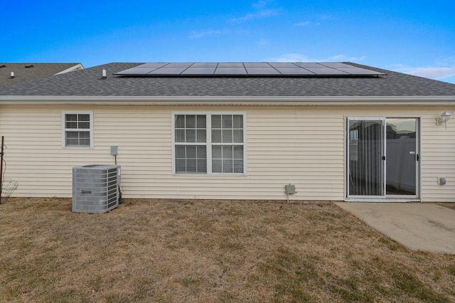 rear view of property featuring central AC, a lawn, and solar panels