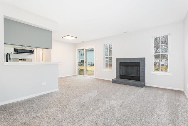 unfurnished living room with a brick fireplace, a healthy amount of sunlight, and light carpet