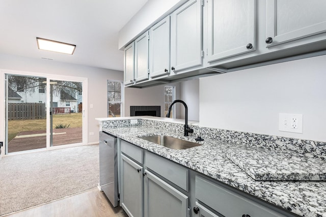 kitchen featuring stainless steel dishwasher, gray cabinets, light stone countertops, and sink