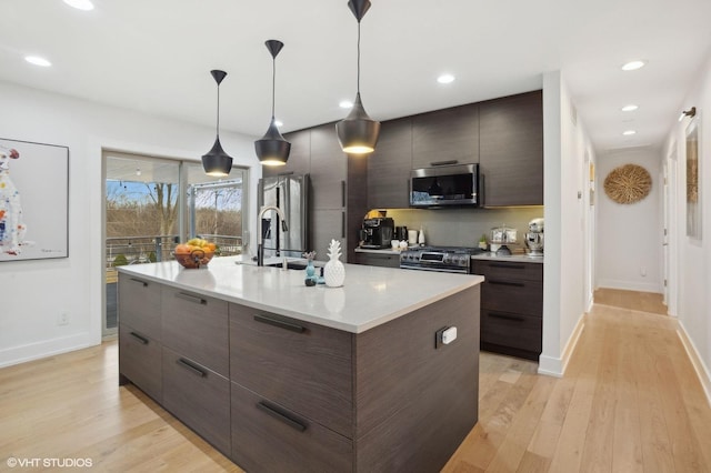 kitchen with dark brown cabinetry, sink, appliances with stainless steel finishes, pendant lighting, and a kitchen island with sink