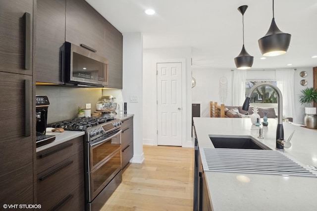 kitchen featuring sink, light wood-type flooring, appliances with stainless steel finishes, pendant lighting, and decorative backsplash