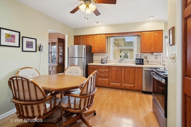 kitchen featuring appliances with stainless steel finishes, tasteful backsplash, sink, ceiling fan, and light wood-type flooring