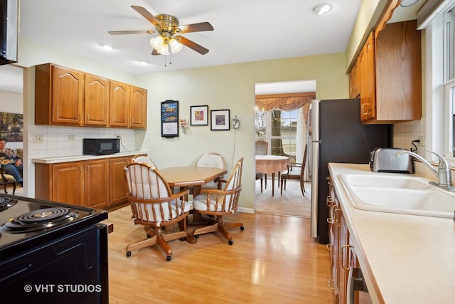 kitchen featuring sink, stainless steel fridge, ceiling fan, tasteful backsplash, and light wood-type flooring