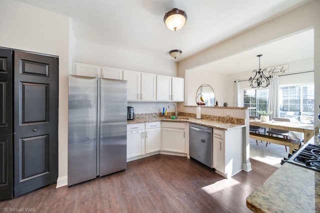 kitchen with sink, appliances with stainless steel finishes, kitchen peninsula, pendant lighting, and white cabinets