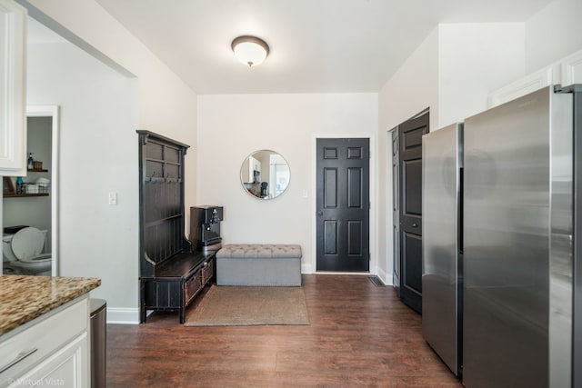 kitchen featuring dark hardwood / wood-style flooring, light stone countertops, white cabinets, and stainless steel refrigerator