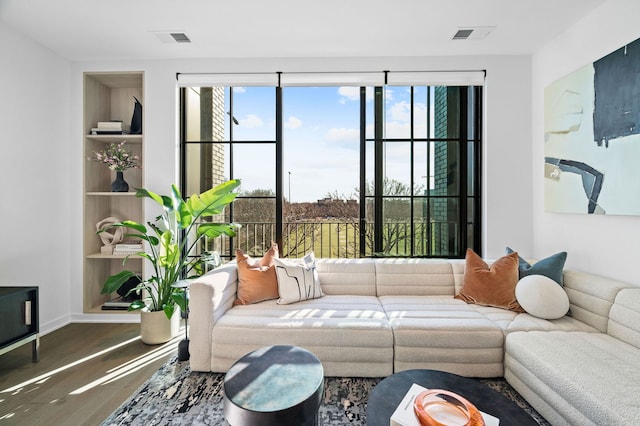 living area featuring baseboards, wood finished floors, visible vents, and built in features