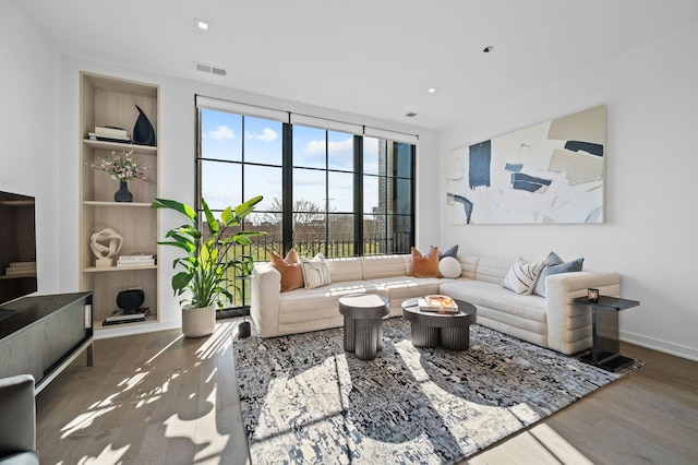 living area featuring baseboards, visible vents, built in features, wood finished floors, and recessed lighting