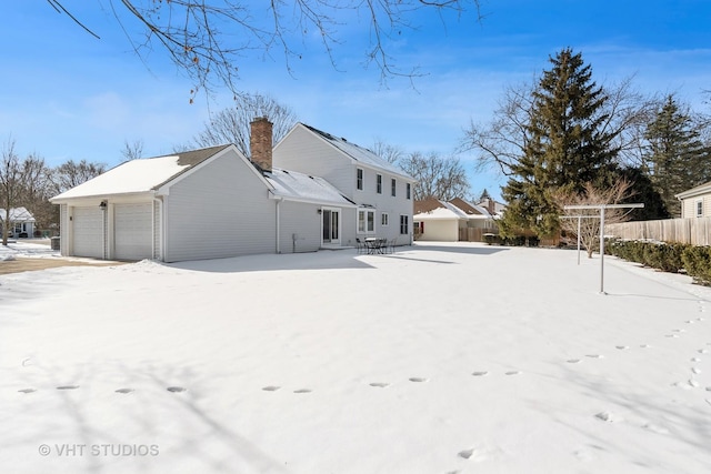 rear view of house with a detached garage, a chimney, and fence