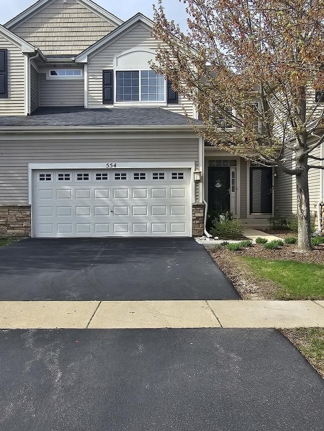 traditional-style house with a garage, a shingled roof, stone siding, and aphalt driveway