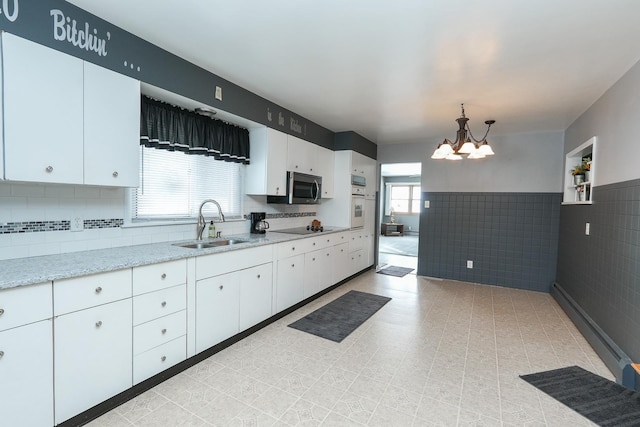 kitchen with white cabinets, a wainscoted wall, stainless steel microwave, hanging light fixtures, and a sink