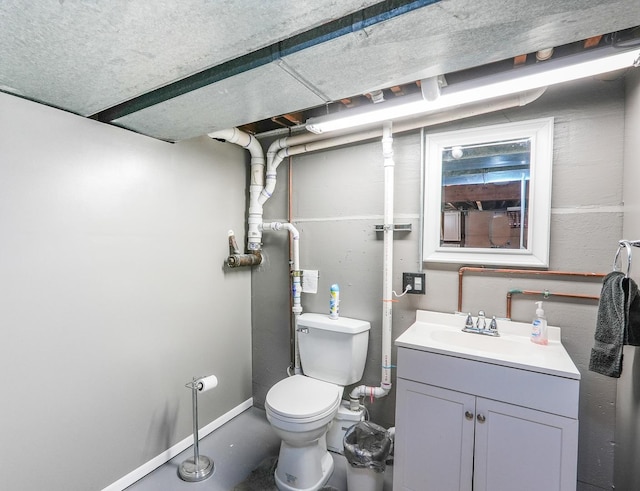 bathroom featuring toilet, baseboards, concrete flooring, and vanity