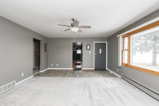 interior space with ceiling fan, light colored carpet, a baseboard heating unit, visible vents, and baseboards