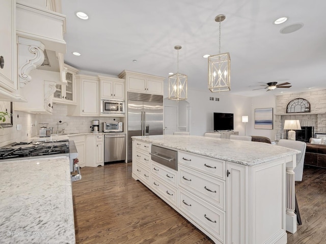 kitchen with backsplash, dark hardwood / wood-style floors, built in appliances, light stone countertops, and decorative light fixtures